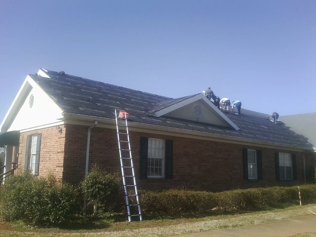 Crew tearing shingles off a brick ranch roof with a ladder set — Emergency Roof Repair work by our crew in Corydon