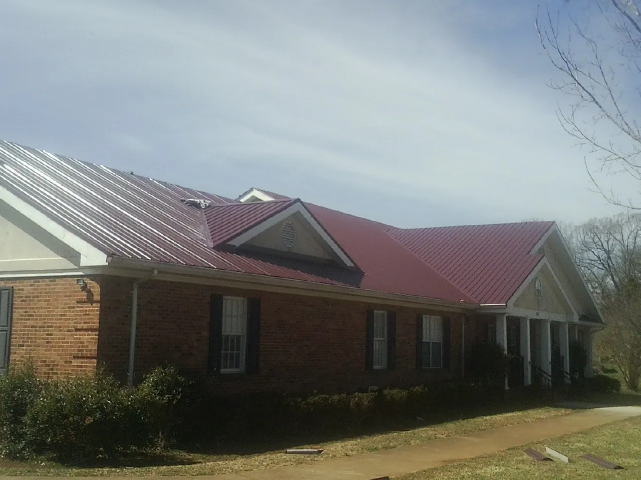 Red metal roof with gabled entries on a long brick building, from a Hail Damage Roof Repair job in Corydon